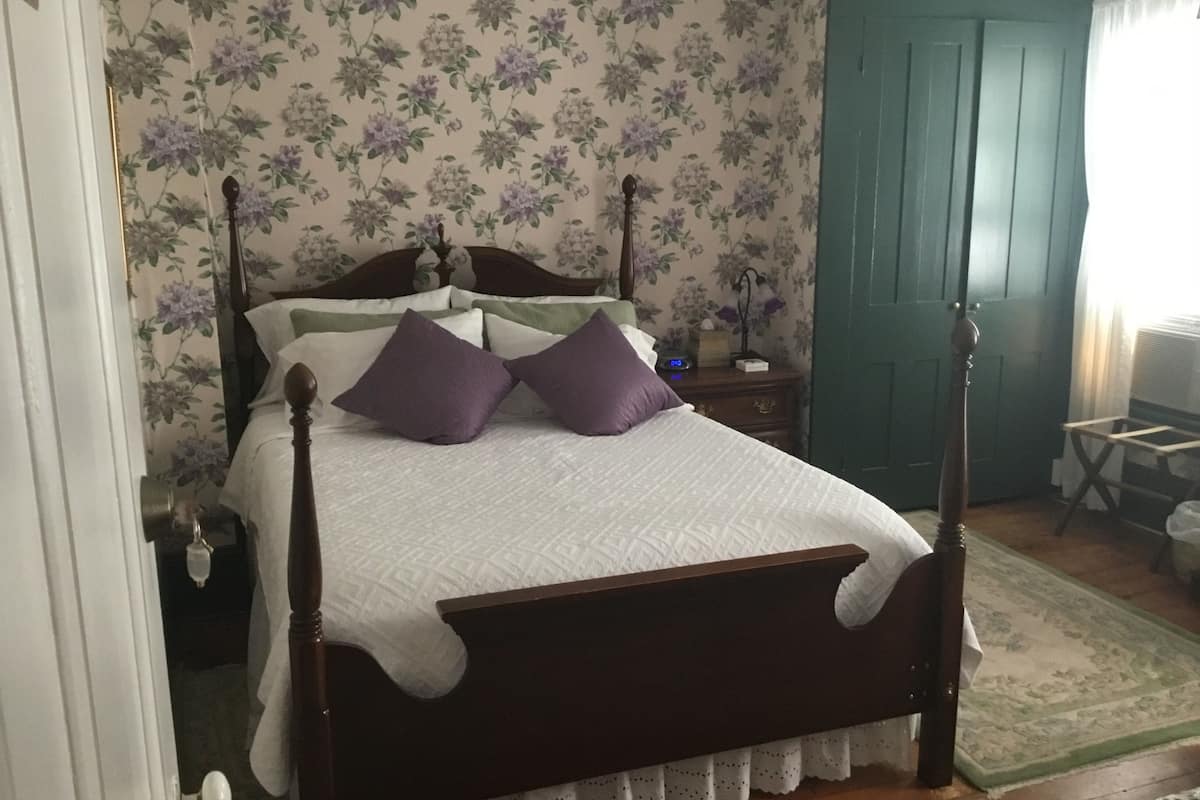 Una camera da letto con un letto a baldacchino, carta da parati floreale, una porta verde e un comodino con una lampada.