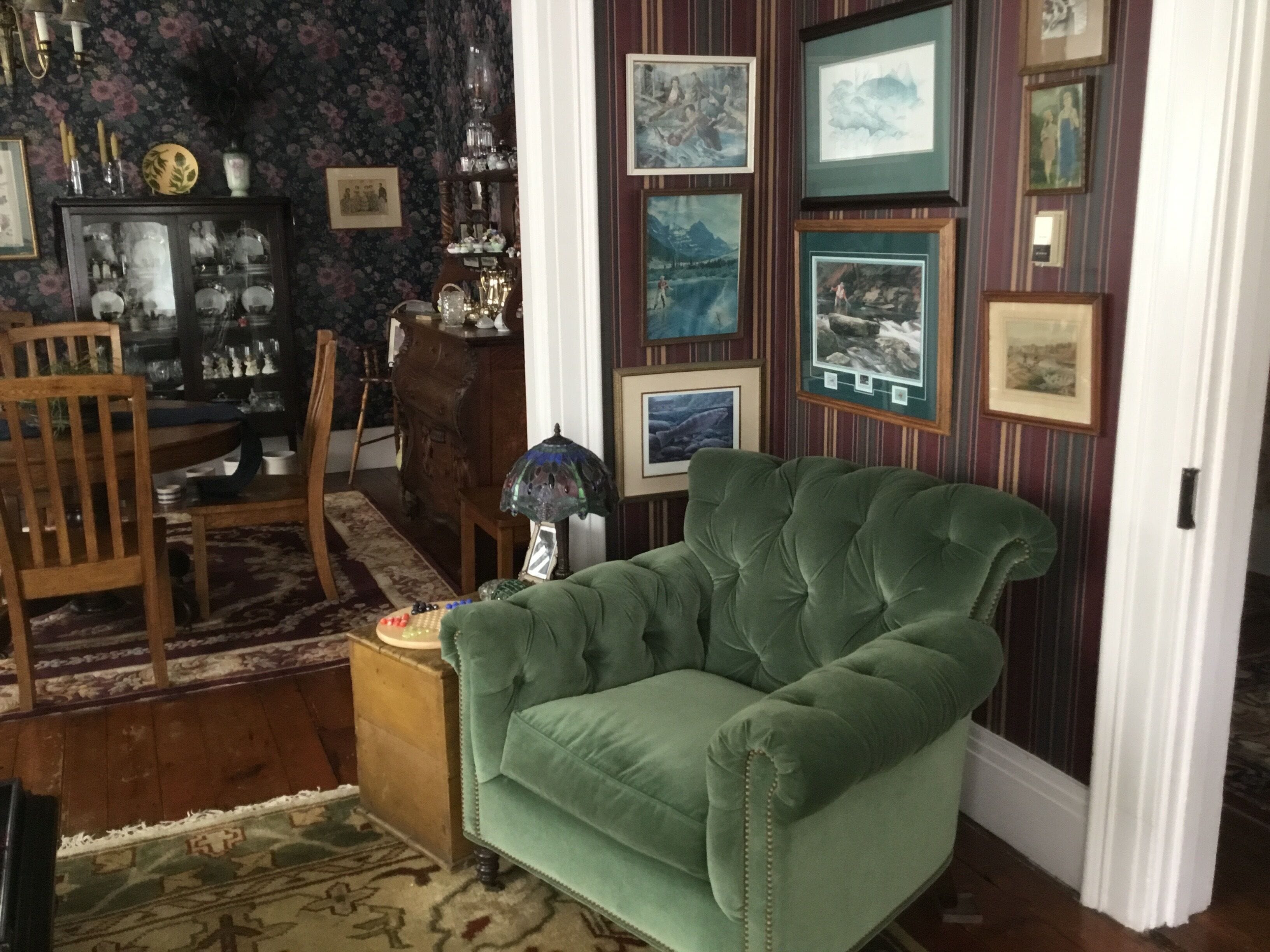 A room with a green sofa, wooden furniture, a patterned rug, and a wall adorned with framed pictures.