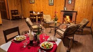 Een eetgedeelte met een rode tafelkleed, houten stoelen, een open haard en een eettafel gedekt met borden, glazen en een fles.