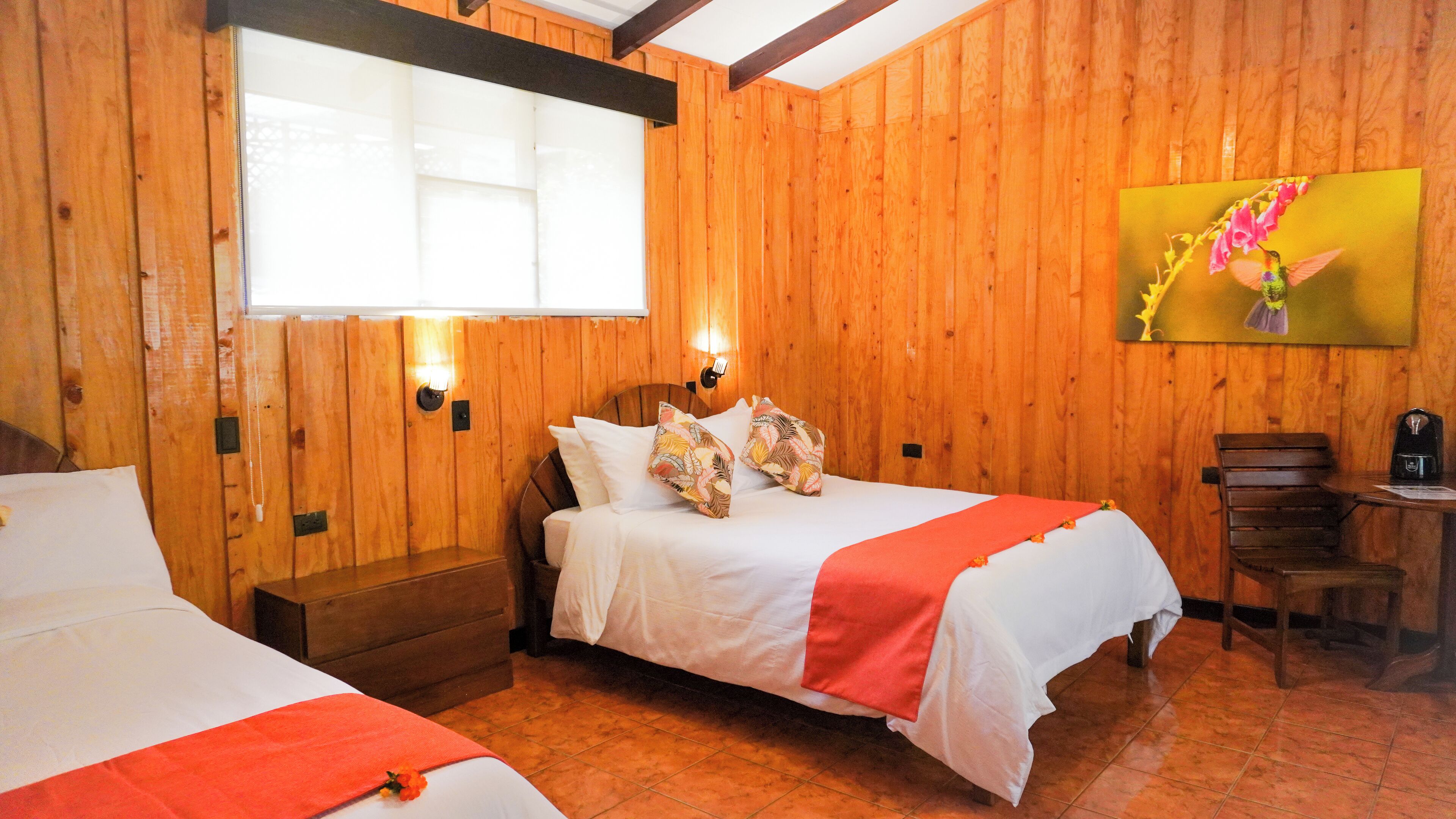 Una habitación con paneles de madera, dos camas, una mesita y un cuadro en la pared.
