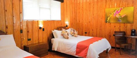 Una habitación con paneles de madera, dos camas, una mesita y un cuadro en la pared.