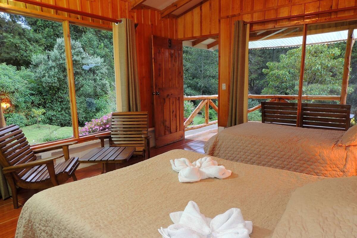 Una habitación de madera con una cama, dos sillas y una ventana con vistas a un jardín.