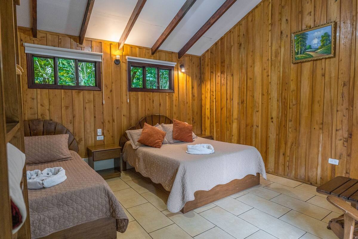 Una habitación de madera con dos camas, un banco y un cuadro en la pared.