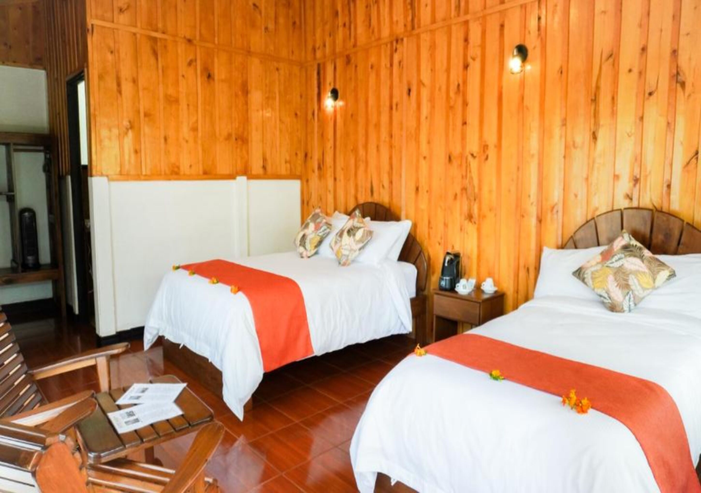 Een hotelkamer met twee bedden, houten wanden, een klein tafeltje met papieren en een nachtkastje met een telefoon.