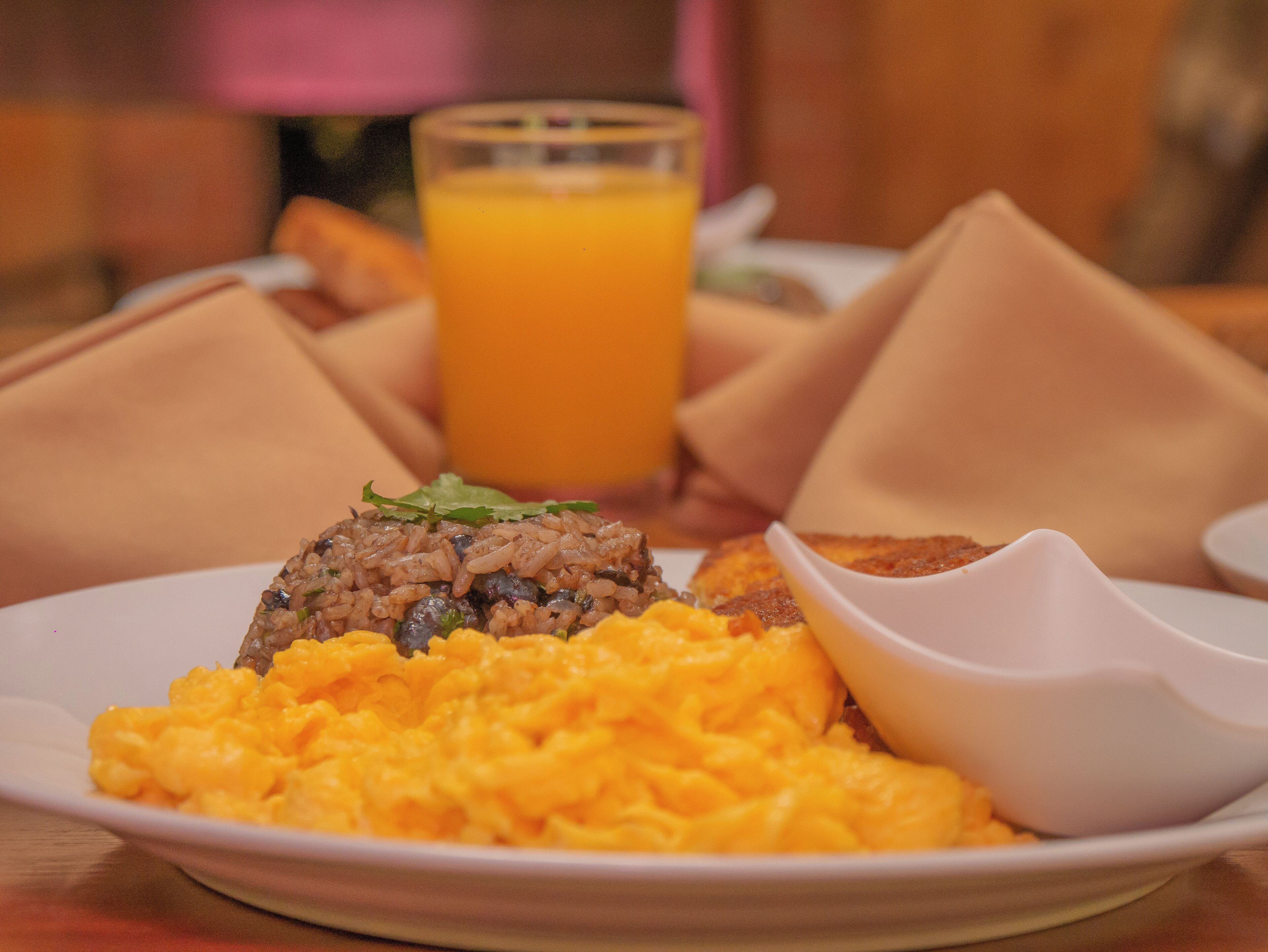 Un plato de comida con huevos revueltos, una hamburguesa y un vaso de jugo de naranja.