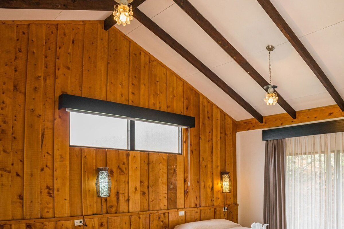 Une chambre avec deux lits, des murs en bois, une fenêtre et un lustre.