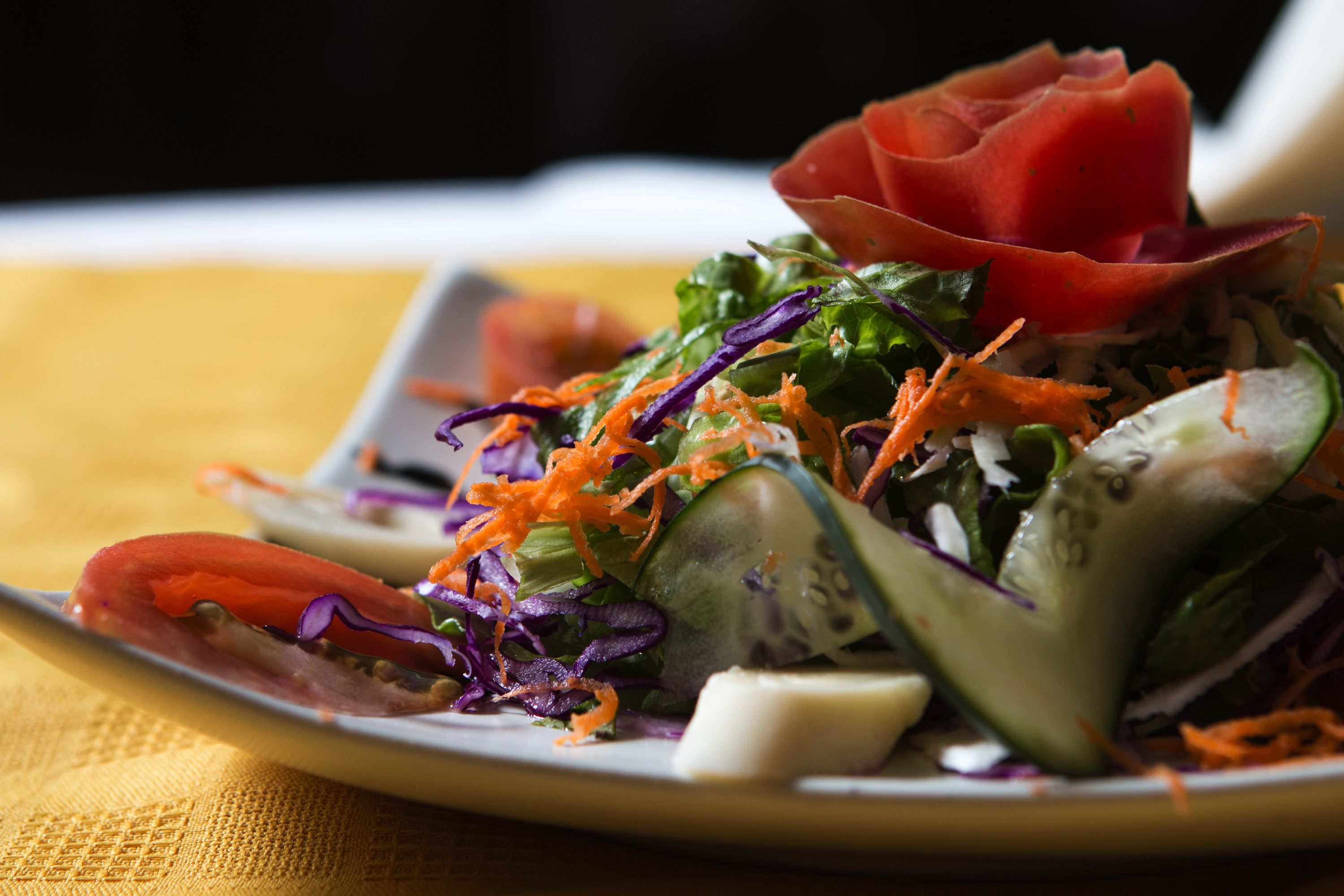 A plate of salad with various vegetables and a decorative red leaf on top.