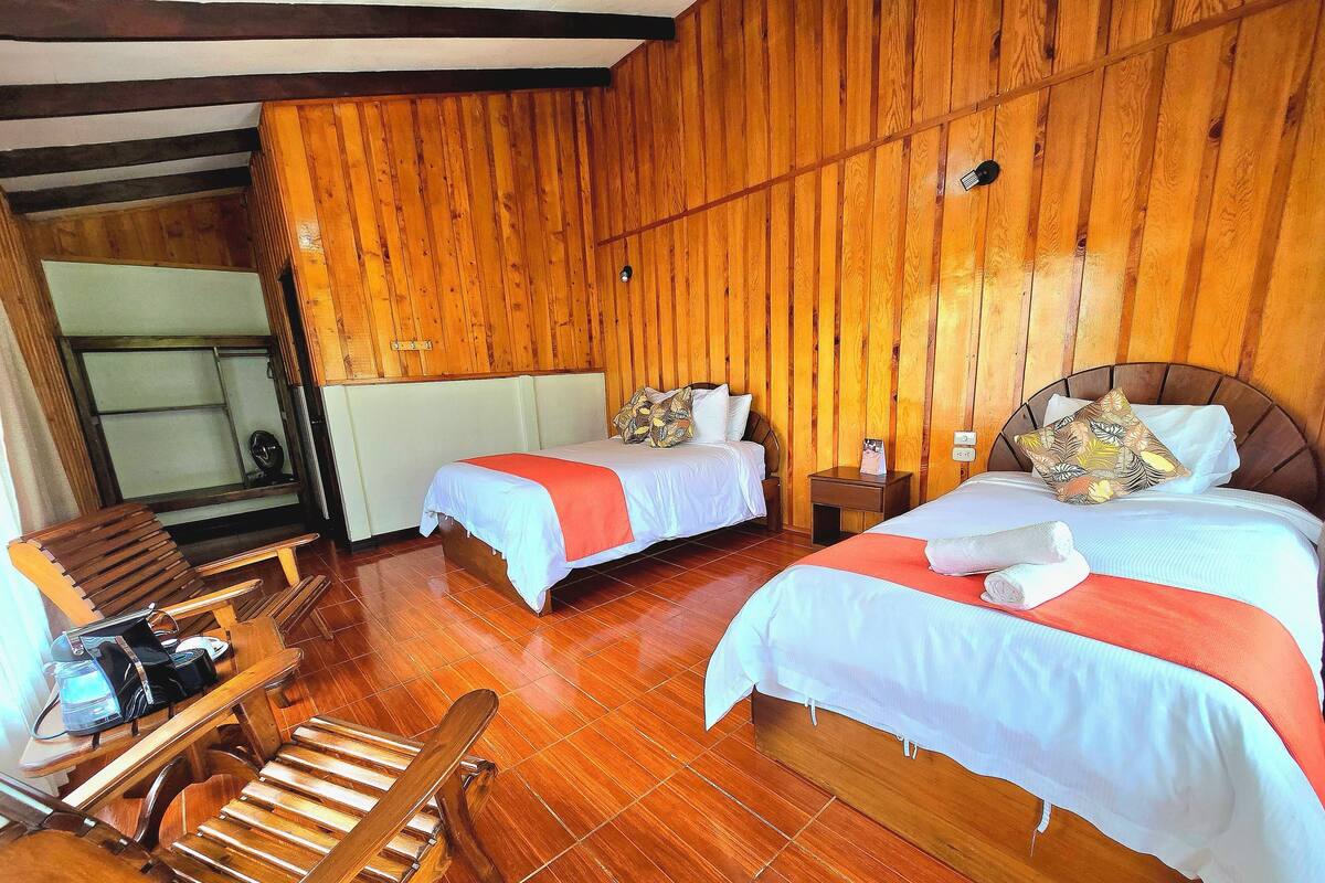 Habitación con dos camas, piso de madera, una silla de madera y una pequeña mesa con una silla.