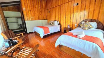 Habitación con dos camas, piso de madera, una silla de madera y una pequeña mesa con una silla.