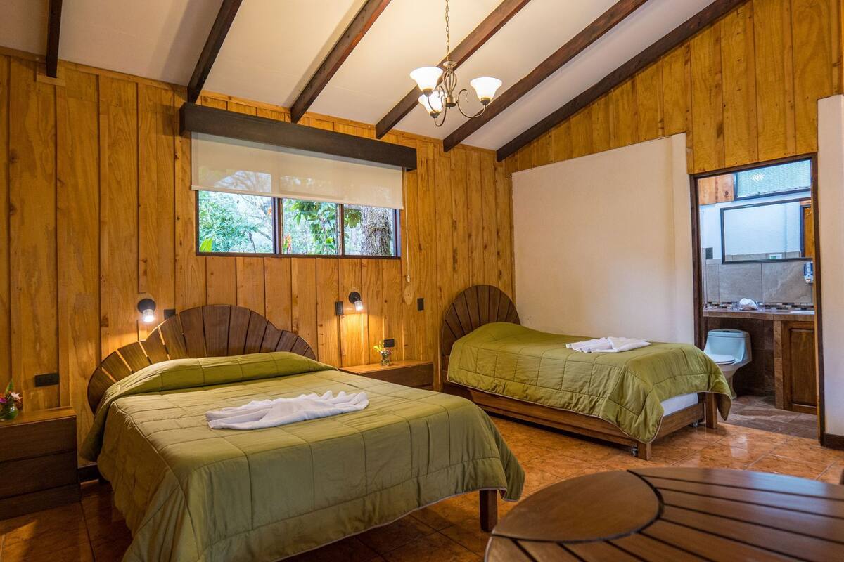 Una habitación con dos camas, paredes de madera, un candelabro, un ventanal con vistas y una pequeña mesa.