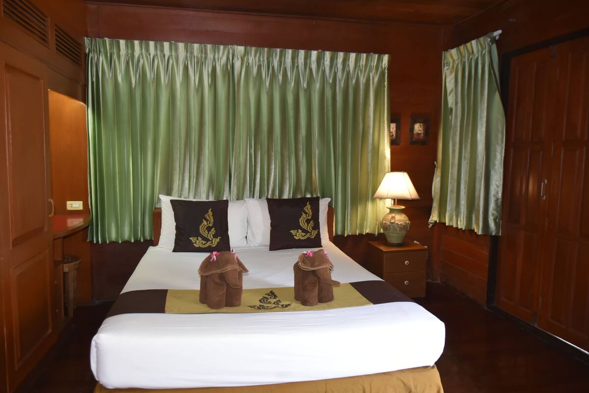 Una habitación de hotel con una cama grande, cortinas verdes, una mesita de noche con lámpara y un armario de madera.