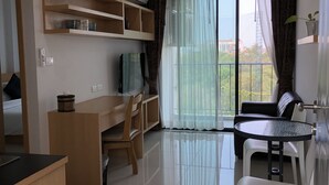 Un salon moderne avec un bureau en bois, un téléviseur et un coin repas comprenant une table et des chaises en verre.