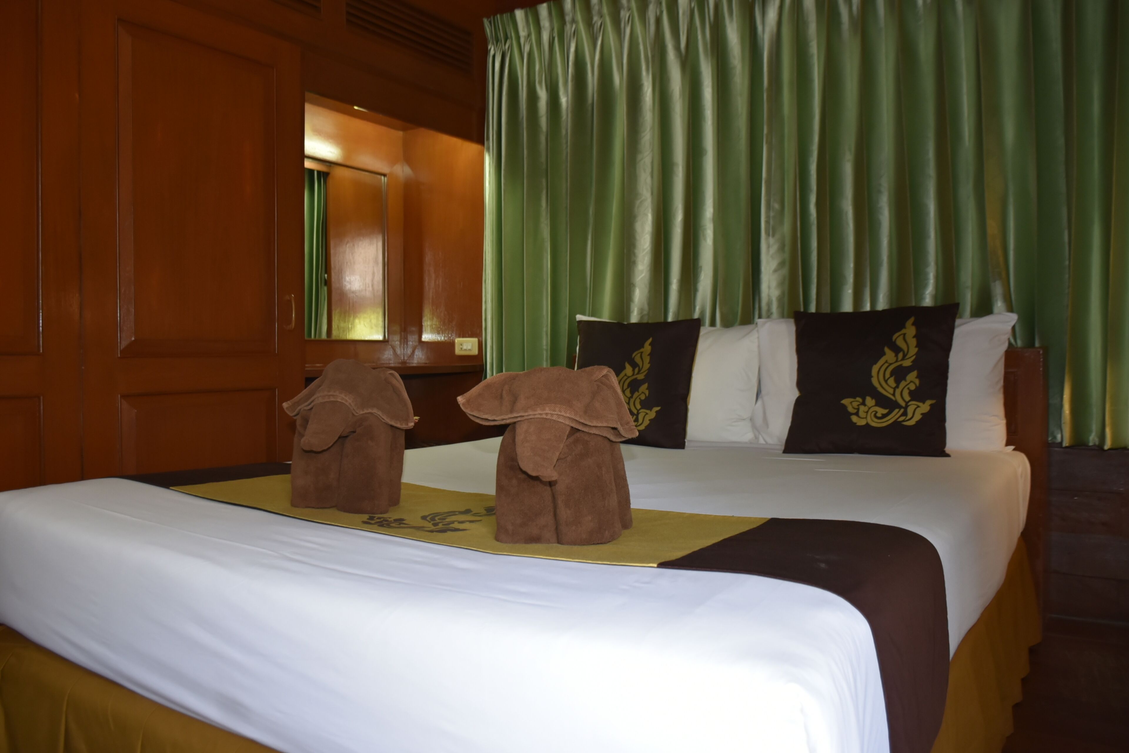 Une chambre d’hôtel avec deux lits, des rideaux verts, un lambris en bois et un coussin décoratif orné d’un emblème doré.