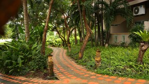 Un sentier pavé de dalles rouges traverse un jardin luxuriant où poussent différentes espèces de plantes et d’arbres.