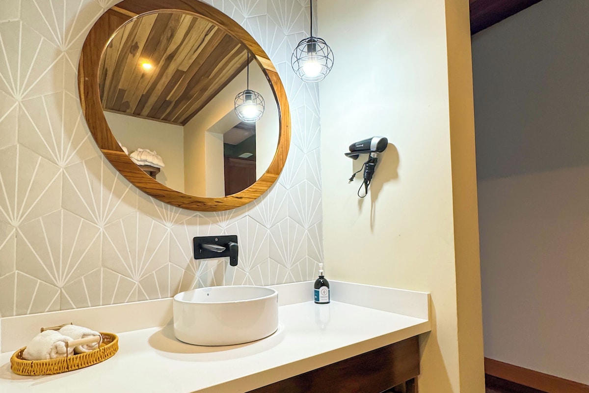 A bathroom with a wooden ceiling, a round mirror, a white sink, and a towel rack.