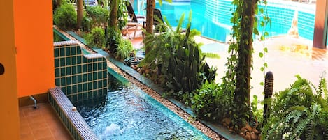 A pool area with a water feature, surrounded by lush greenery and lounge chairs.