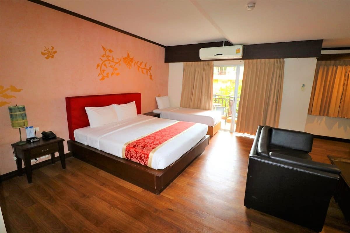 Ein Hotelzimmer mit einem großen Bett, einem kleineren Bett, einem Schreibtisch mit Lampe und einem Sessel.