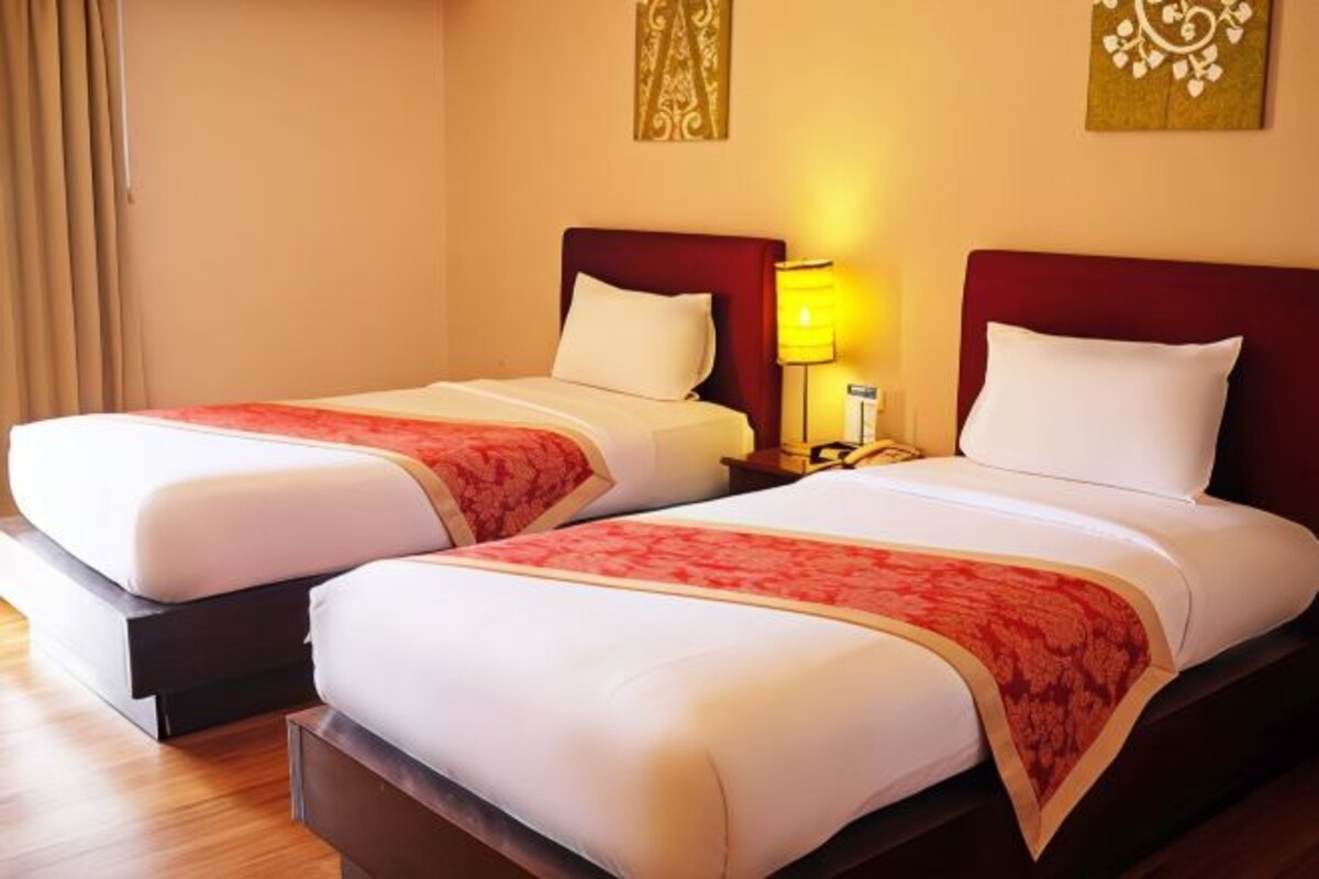 A hotel room with two beds, each with a red and white bedspread, a wooden headboard, and a nightstand with a lamp.
