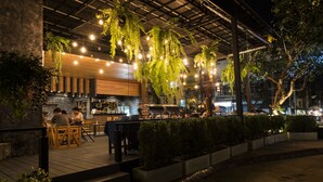 An outdoor restaurant with wooden tables and chairs, hanging plants, and string lights. - Mind Resort Pattaya (Pattaya)