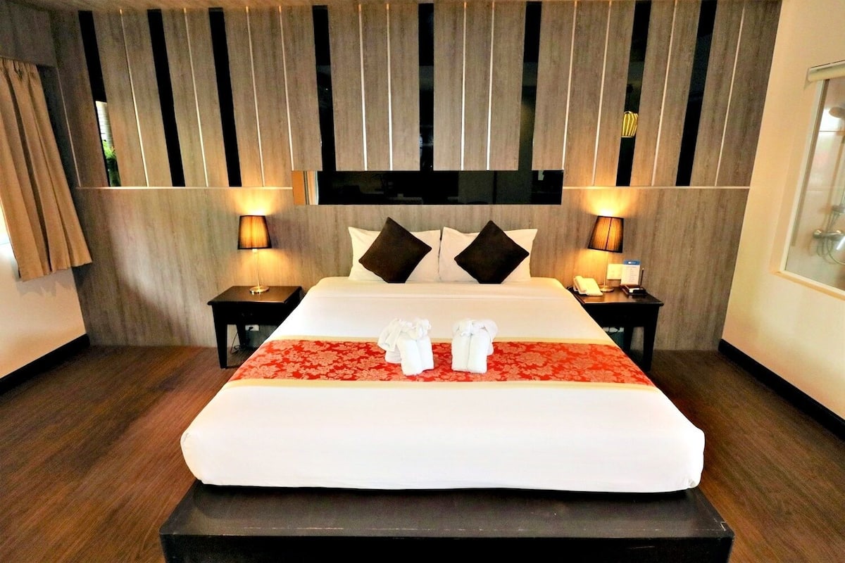 Ein Hotelzimmer mit einem großen Bett, zwei Nachttischen, einem Holzkopfstück und einer roten, blumigen Bettdecke.