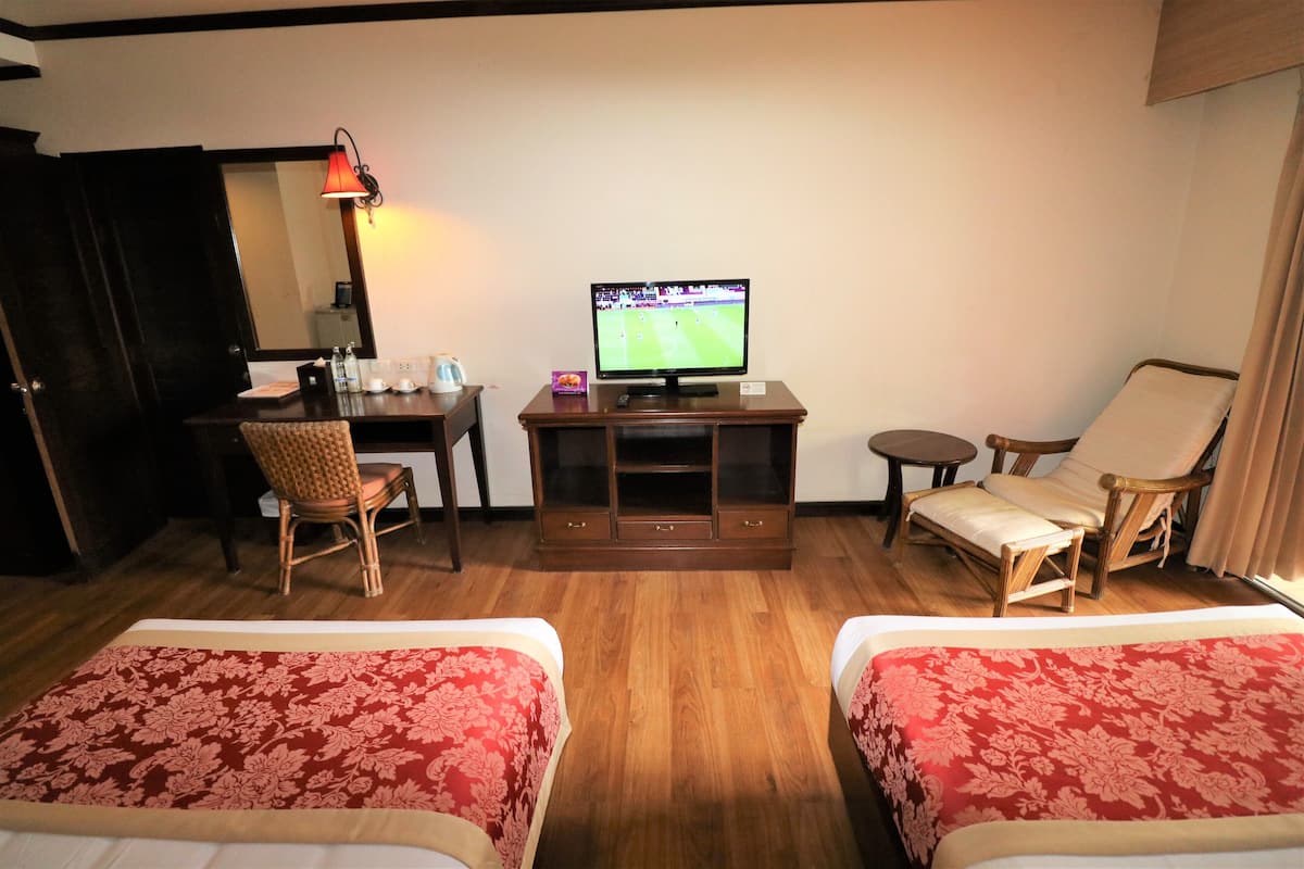 Ein Hotelzimmer mit zwei Betten, einem Schreibtisch, einem Fernseher, einem Sessel und einem kleinen Tisch.