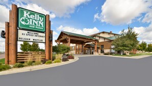 A hotel entrance with a sign for Kelly Inn and Suites, featuring a modern architectural style with a covered entrance and landscaped surroundings. - Kelly Inn & Suites Mitchell South Dakota (Mitchell)