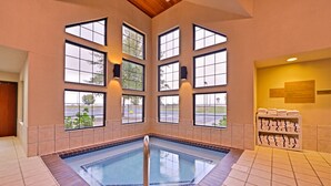 A large indoor swimming pool with multiple windows, a tiled floor, and a towel rack with folded towels. - Kelly Inn & Suites Mitchell South Dakota (Mitchell)