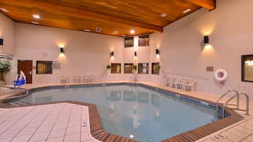 An indoor swimming pool with a wooden ceiling, tiled floor, and multiple chairs around the pool.