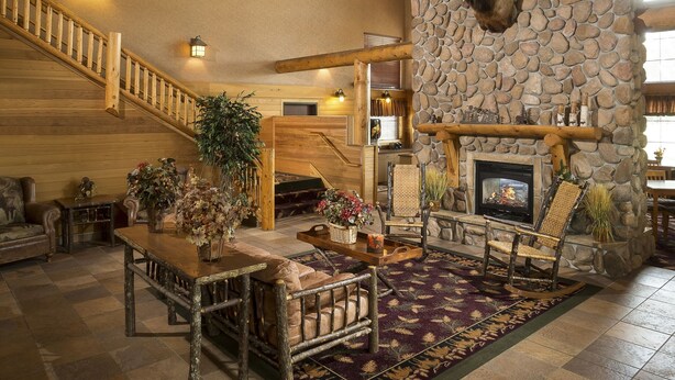 A spacious living area with a stone fireplace, wooden ceiling, and a staircase. - Kelly Inn & Suites Mitchell South Dakota (Mitchell)