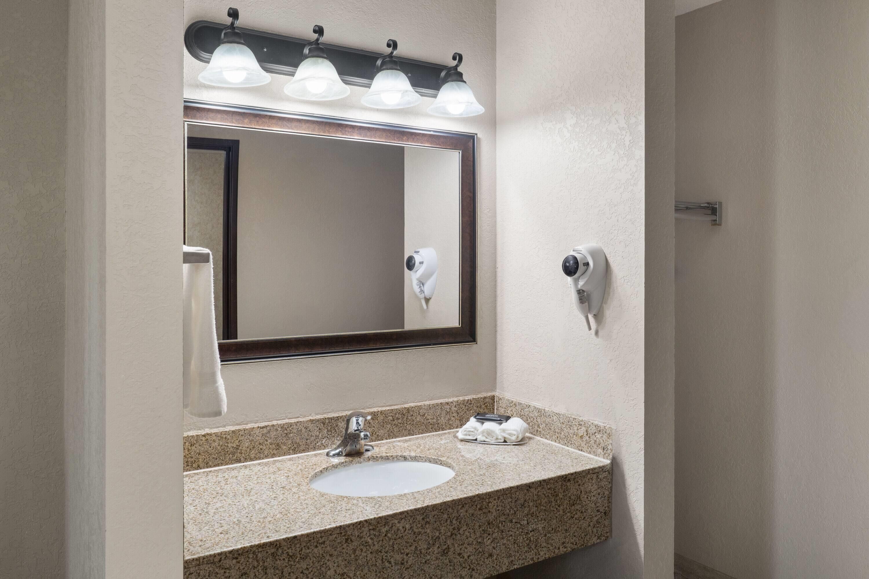 A bathroom with a sink, mirror, towel dispenser, and hairdryer.