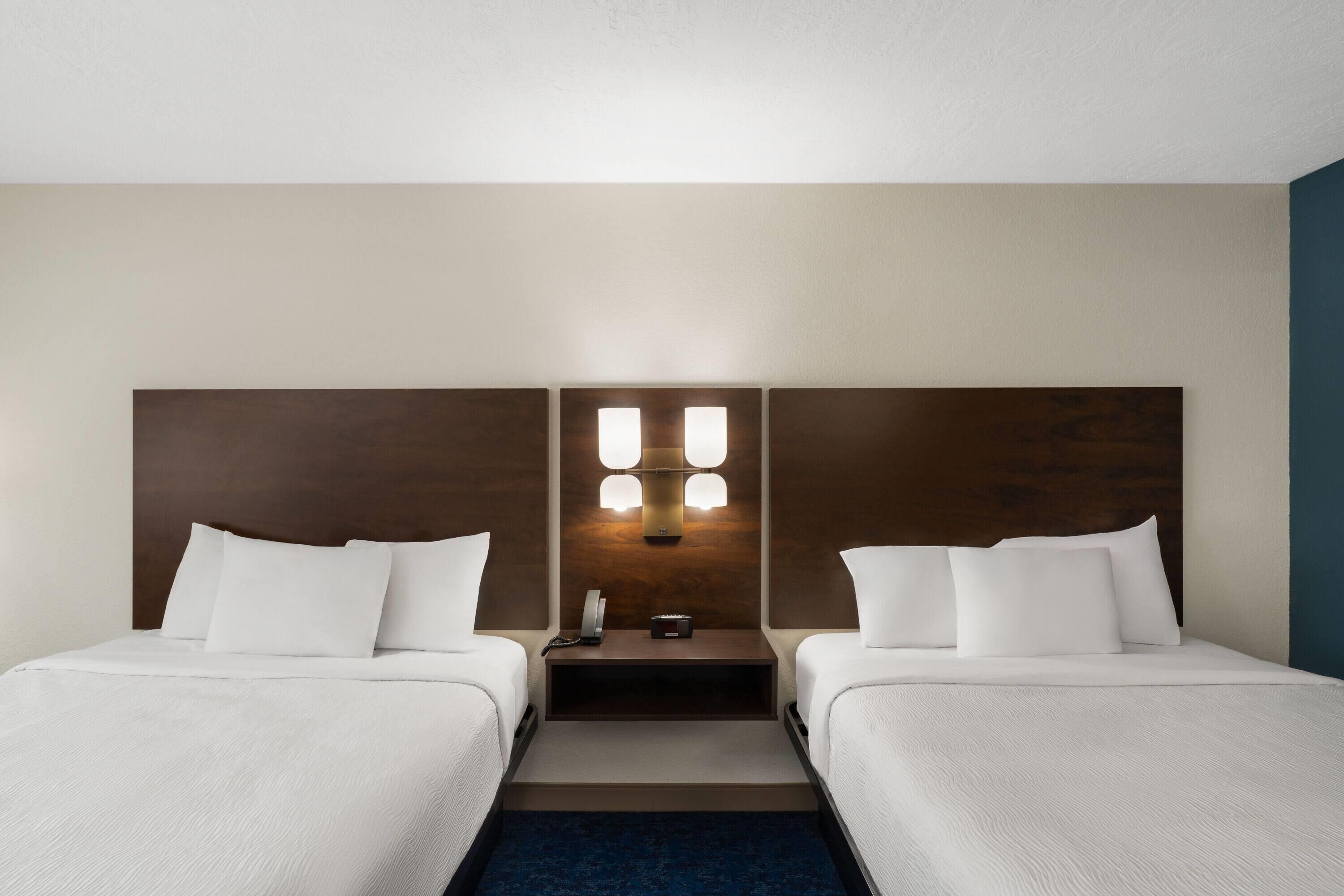 Une chambre d’hôtel avec deux lits, une table de chevet, un luminaire fixé au mur et un téléphone.