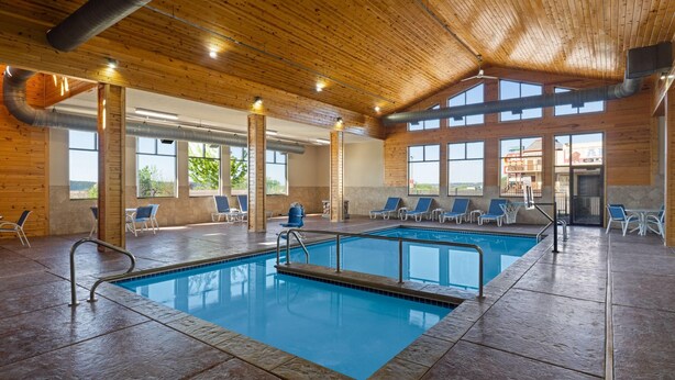 An indoor swimming pool with clear views of the outside, wooden ceiling, and lounge chairs.