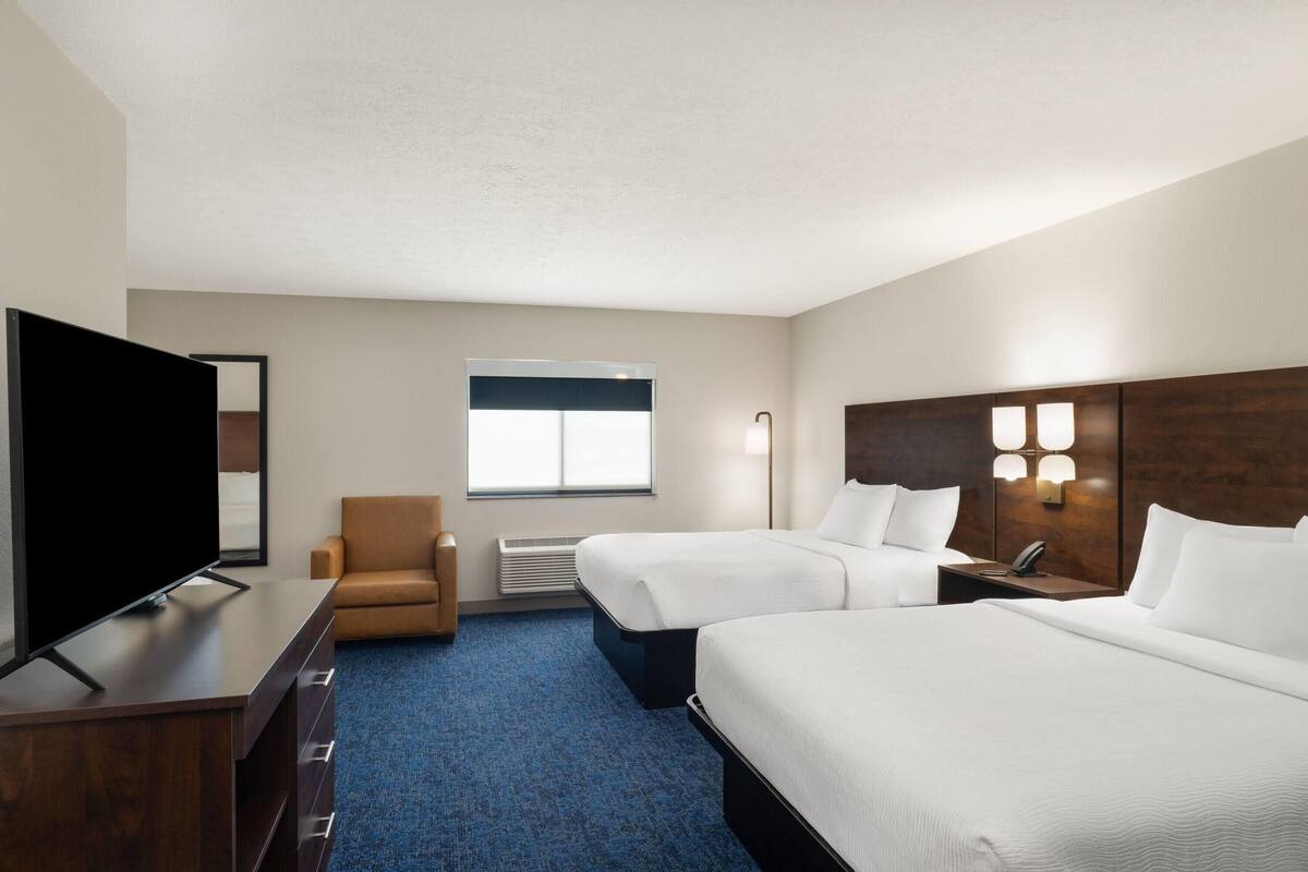 A hotel room with a TV, two beds, a desk, a chair, and a window.
