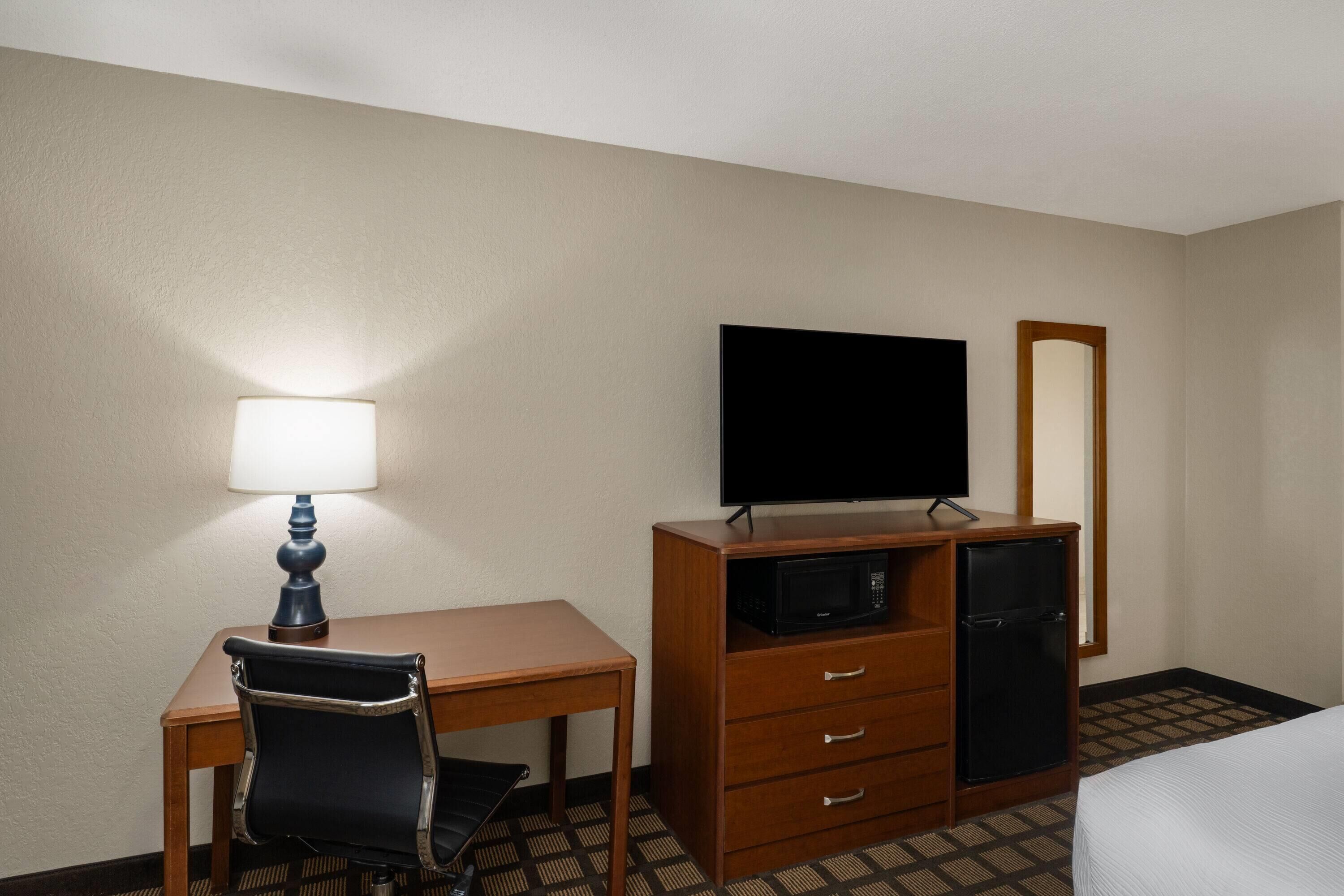Una habitación de hotel con escritorio, silla, televisor, cómoda y cama.