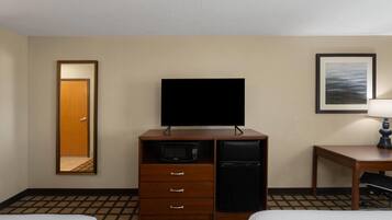 Ett hotellrum med en säng, en TV, en mikrovågsugn, ett kylskåp, ett skrivbord och en spegel.