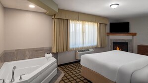 A hotel room with a bathtub, a bed, a fireplace, and a television.