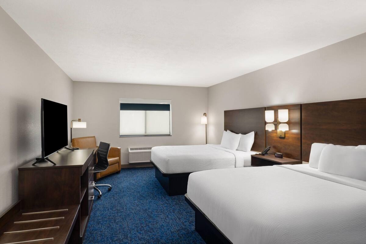 A hotel room with a desk, two beds, a TV, and a window.