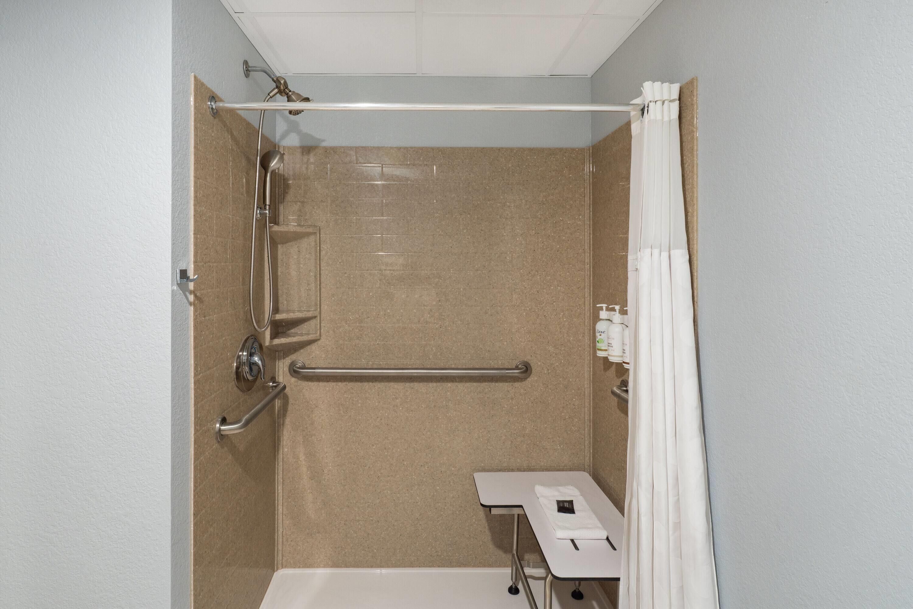 Une salle de bain équipée d’une douche, de barres d’appui, d’un lavabo blanc et d’un porte-serviettes.
