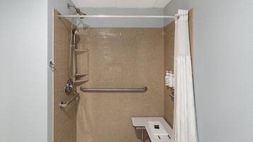 Une salle de bain équipée d’une douche, de barres d’appui, d’un lavabo blanc et d’un porte-serviettes.