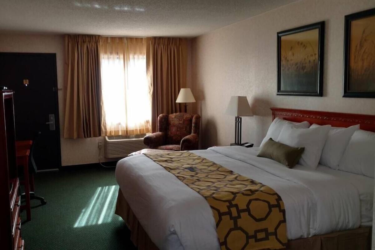 A hotel room with a bed, a chair, a desk, a lamp, and a window with curtains.