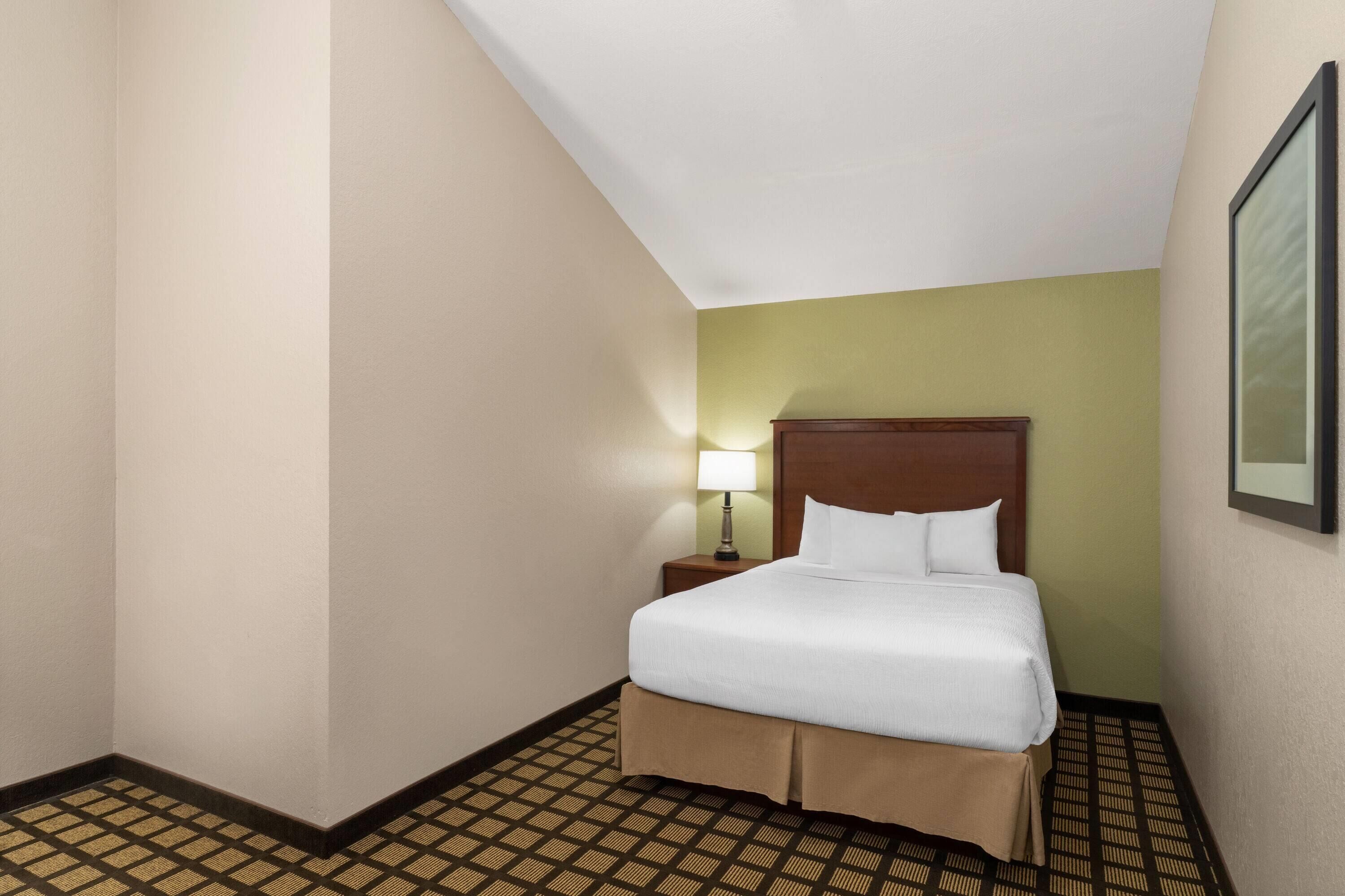 A hotel room with a bed, a nightstand, a lamp, and a patterned floor.