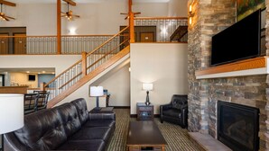 A spacious living area with a fireplace, leather sofa, and a staircase leading to an upper level.