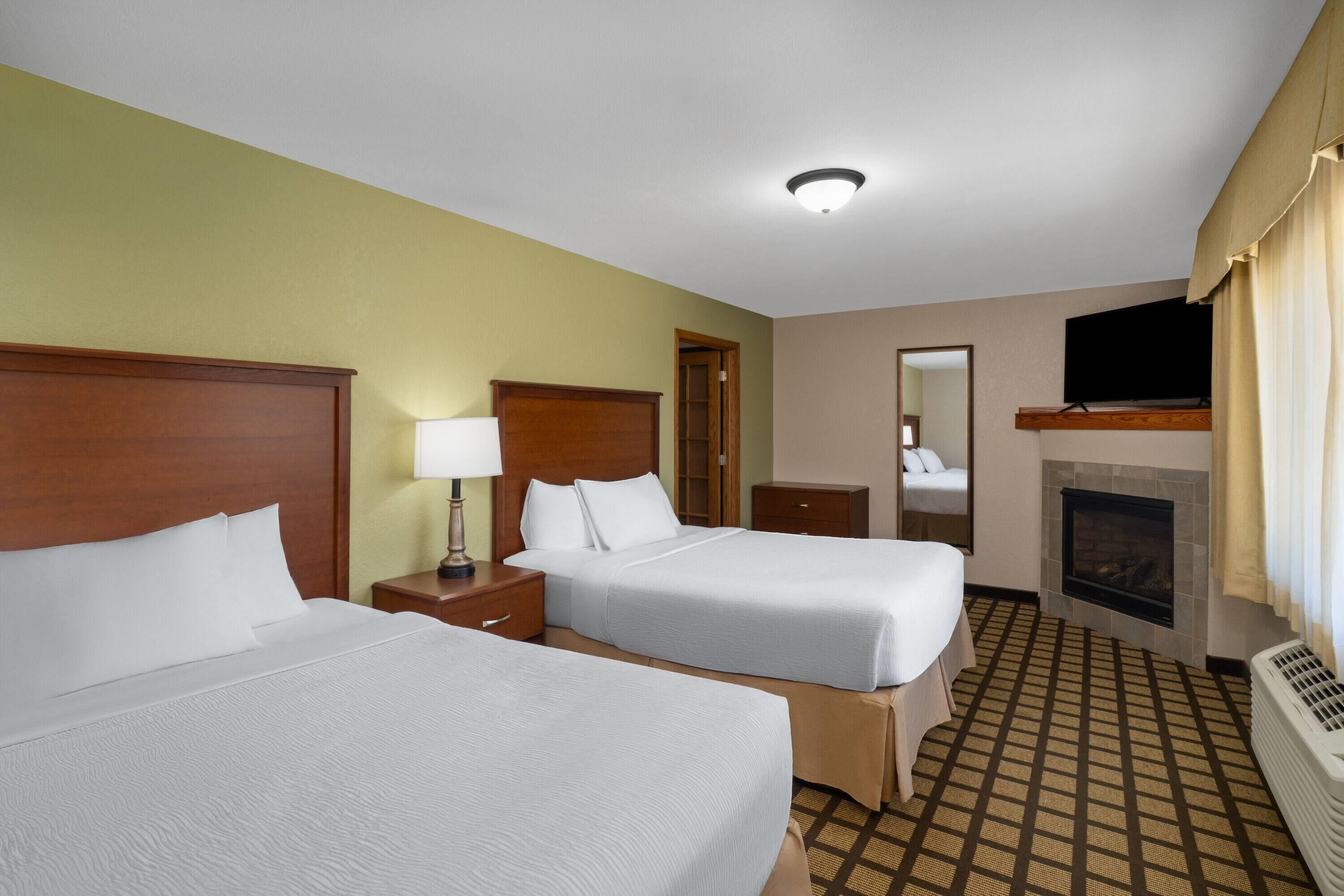 A hotel room with two beds, a television, a fireplace, and a mirror.