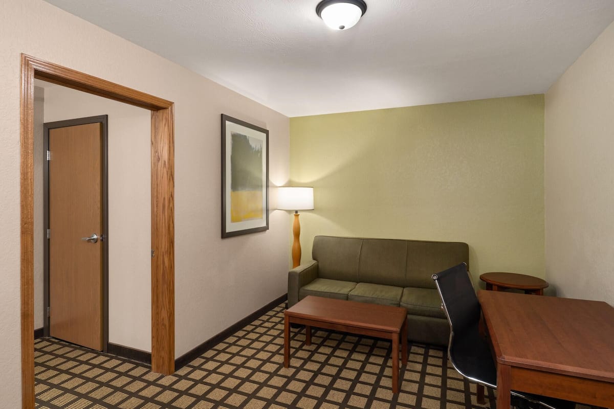 A hotel room with a wooden door, a sofa, a small table, a lamp, and a patterned floor.