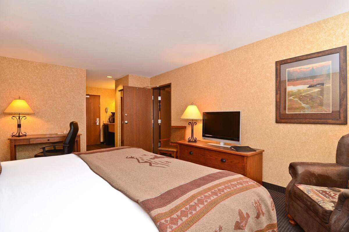 A hotel room with a bed, desk, chair, television, and a painting on the wall.