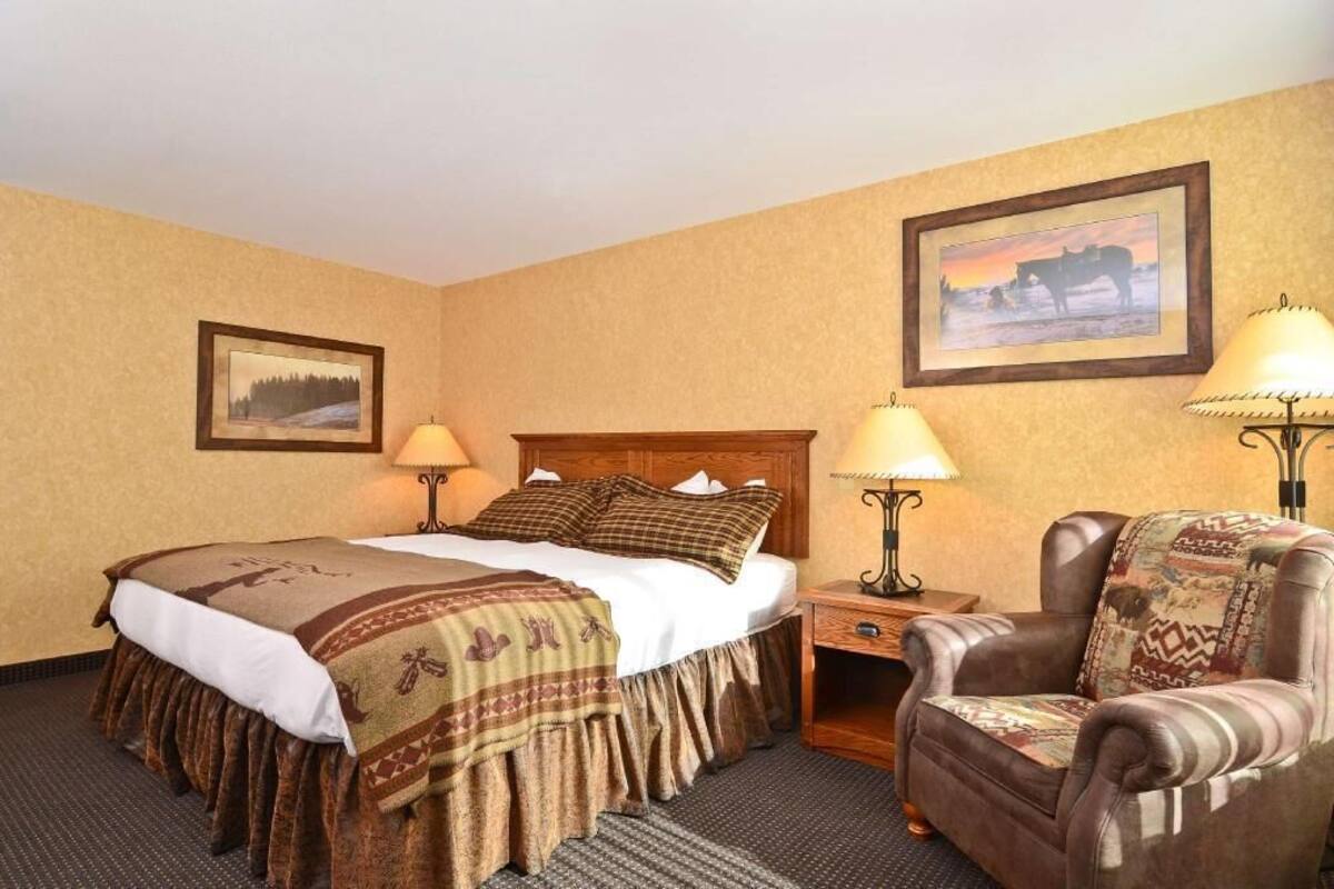 A hotel room with a bed, two bedside lamps, a chair, a rug, and two framed pictures on the walls.