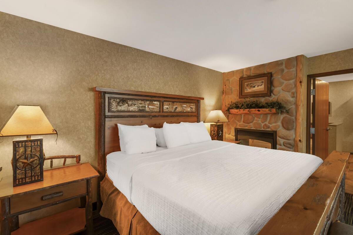 A neatly arranged bedroom with a large bed, a wooden nightstand, a desk, and a stone accent wall.