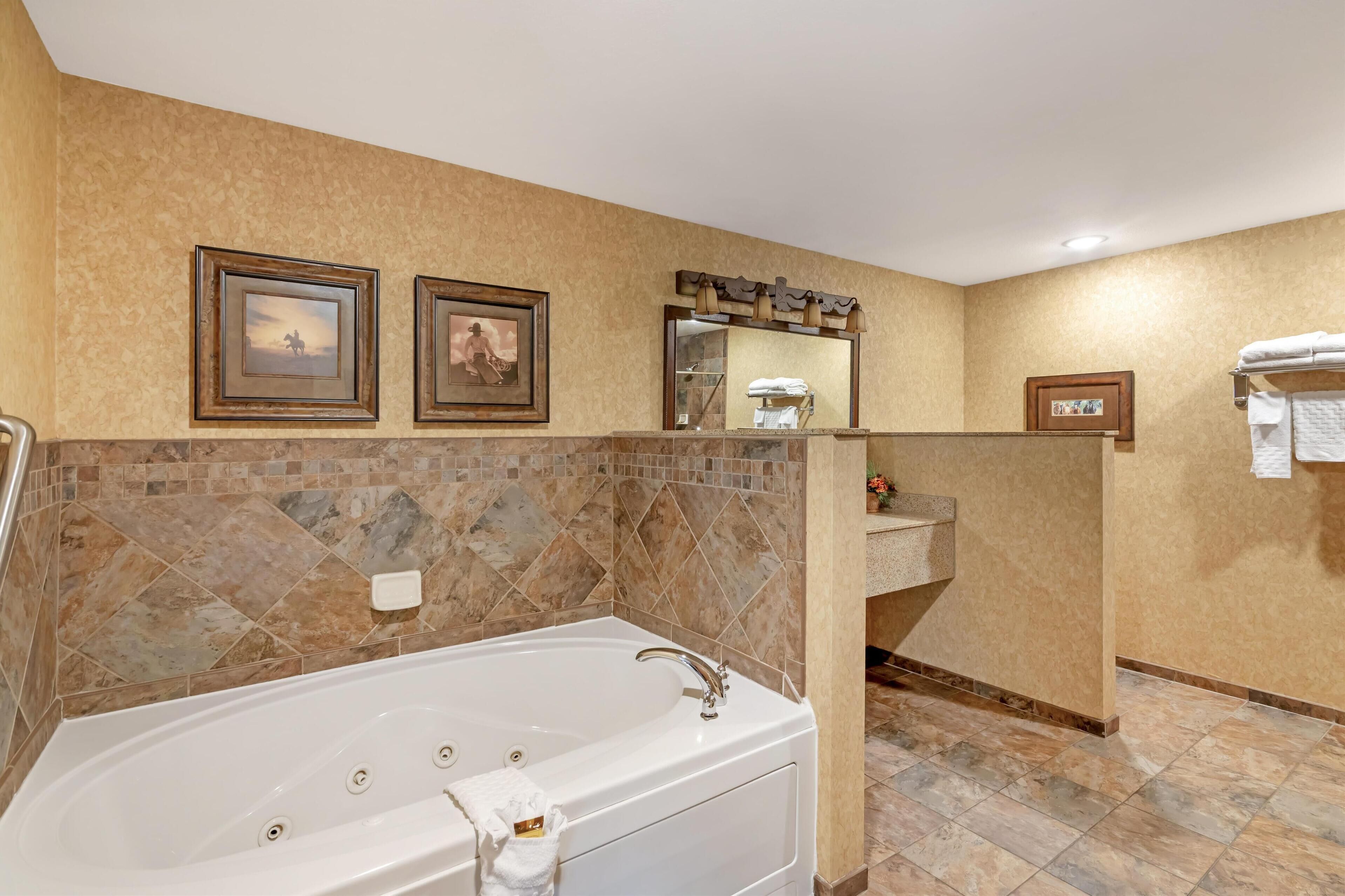 A bathroom with a large bathtub, a vanity with a mirror, and two framed pictures on the wall.