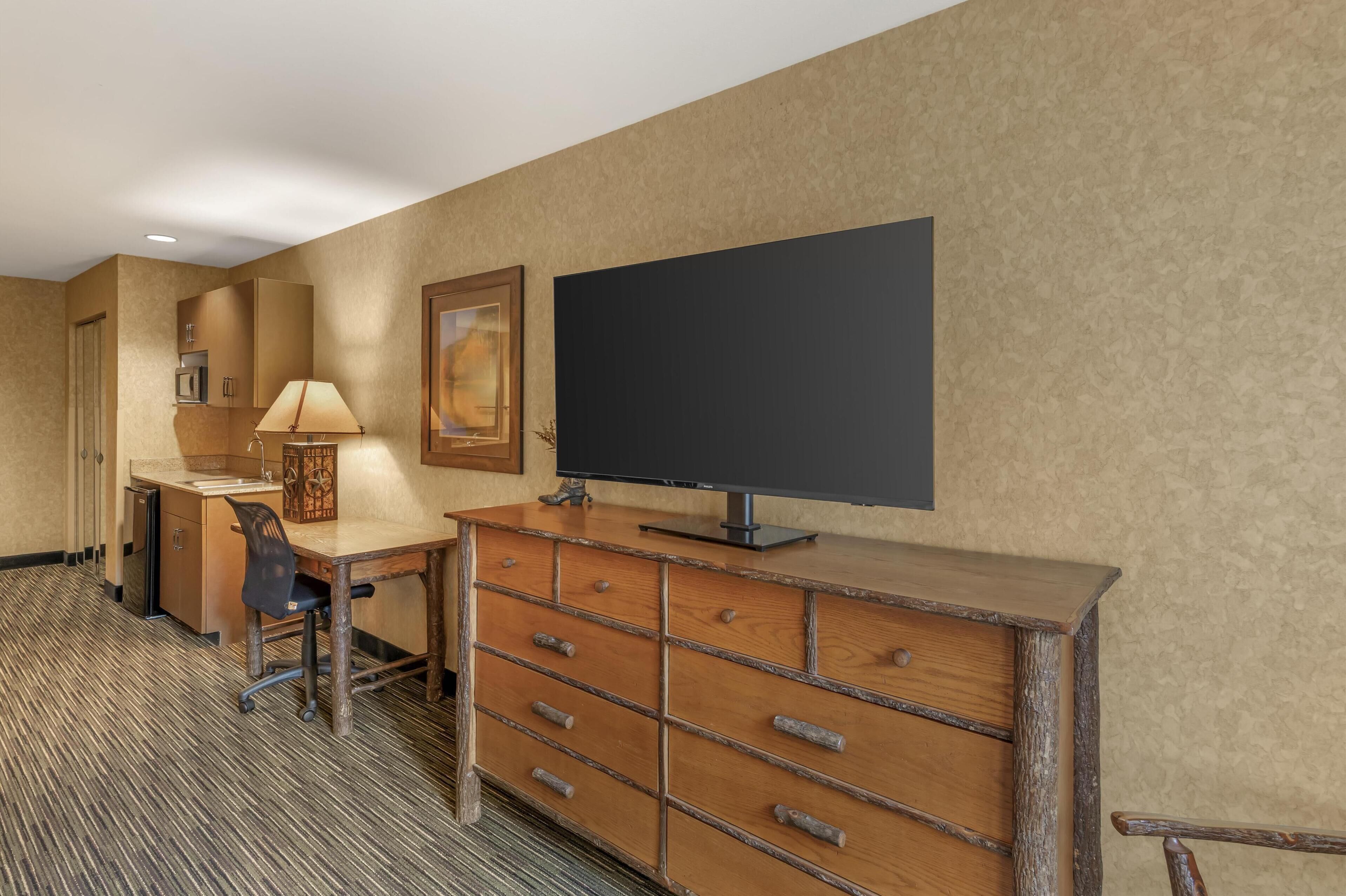 A hotel room with a wooden desk, a television, a lamp, and a framed picture on the wall.