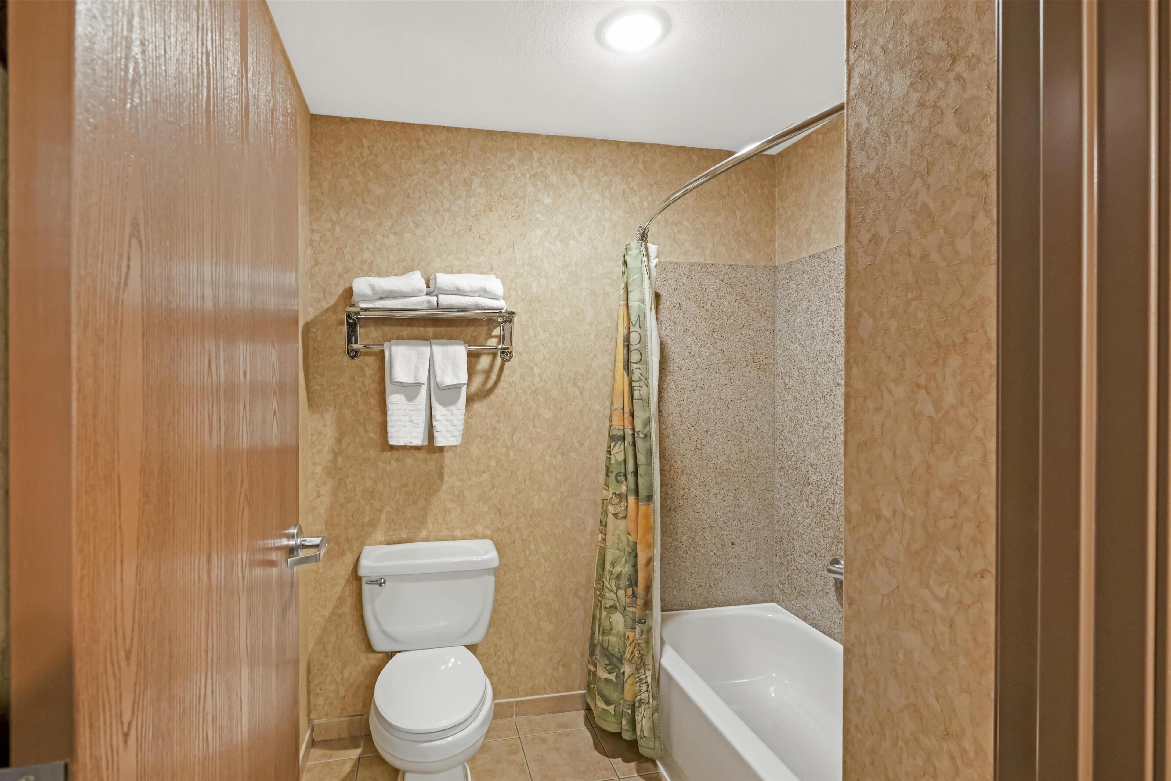 A bathroom with a toilet, a towel rack with towels, a shower with a curtain, and a bathtub.